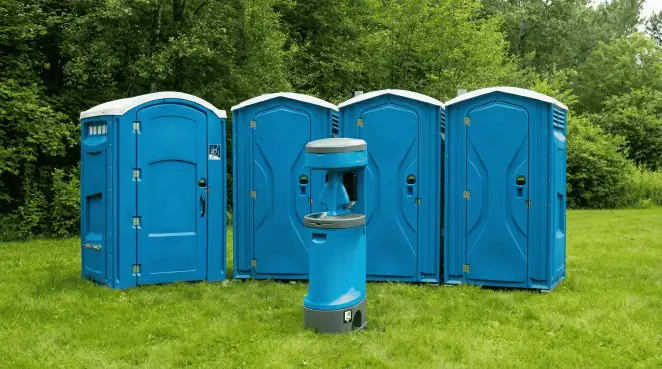 Four blue portable toilets and a matching hand washing station on grass near trees, a common sight at local outdoor events in ,